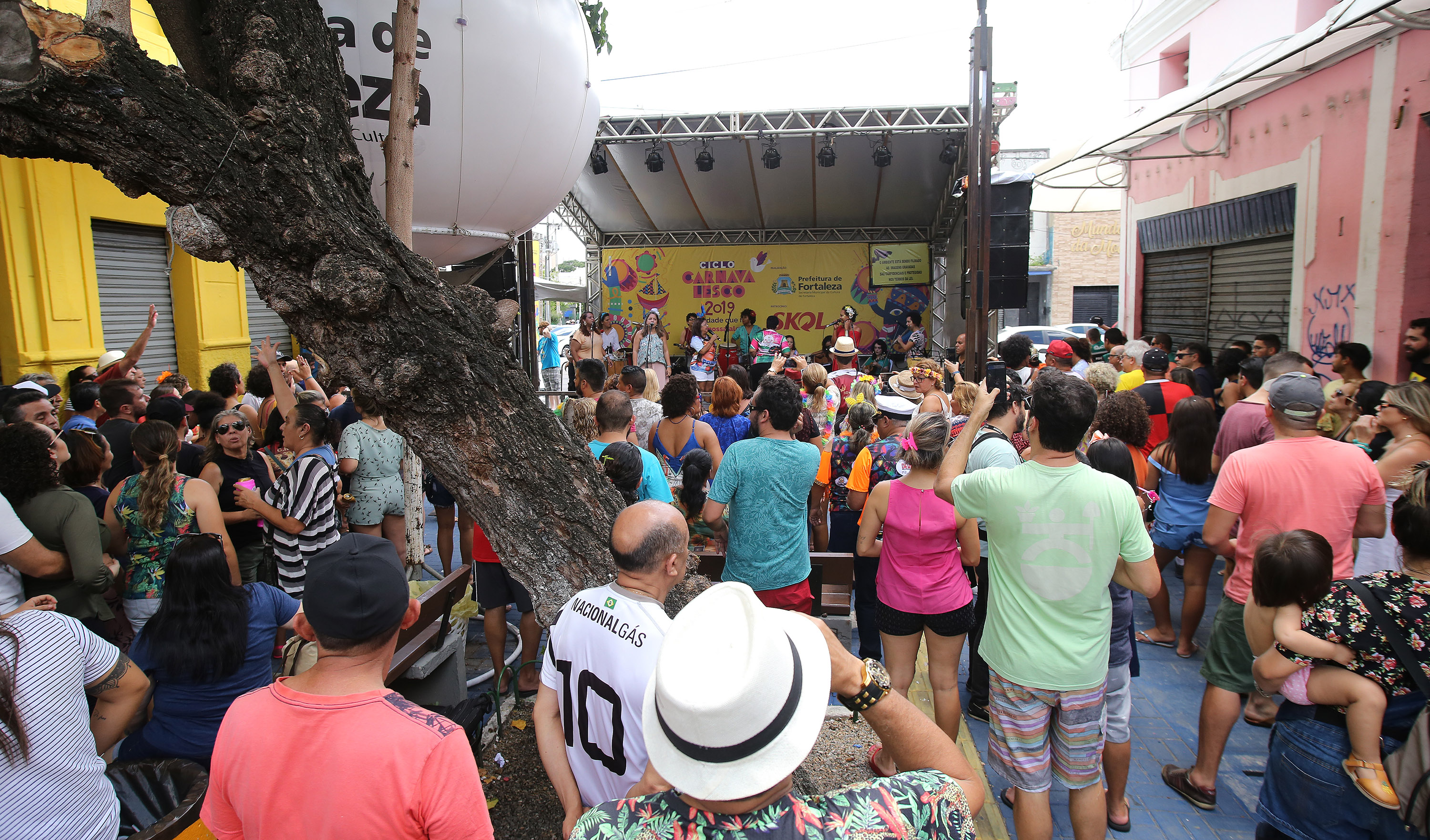 várias pessoasna frente de um palco onde se apresenta um grupo de cantoras